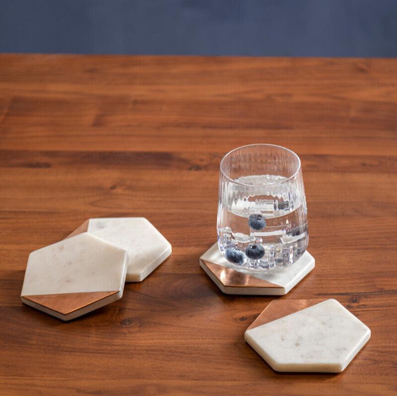 A set of 4 marble coasters on a tabletop, with a glass on one of the coasters