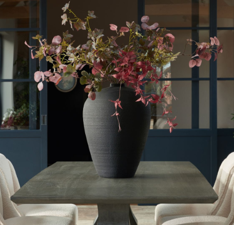 A large matt black vase with autumnal flowers in it, on a table.
